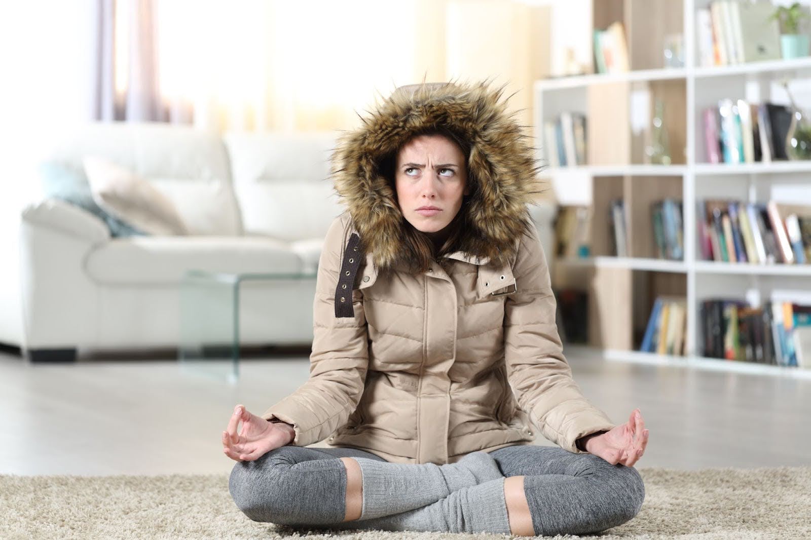 woman who is wearing a coat inside as she does yoga because her furnace is broken