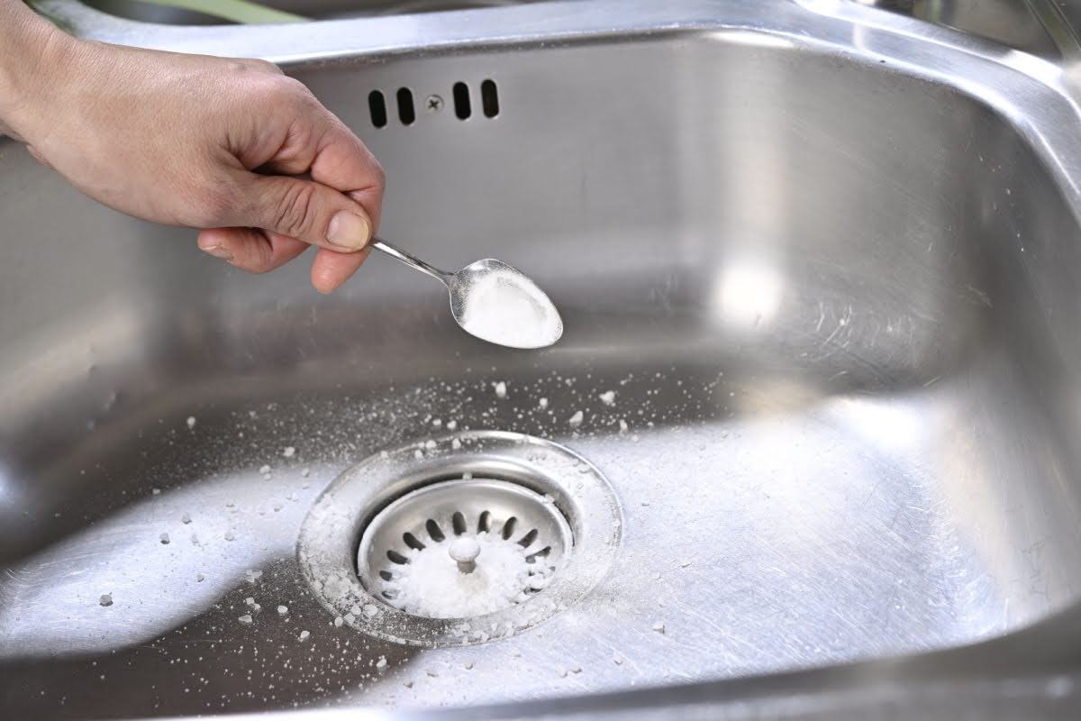 A male hand sprinkling baking soda into a kitchen sink drain