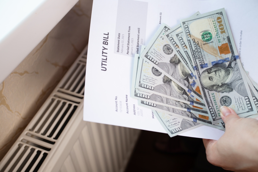 heating bill and hundreds of dollars in cash in front of a radiator to show the expense of skipping heating maintenance