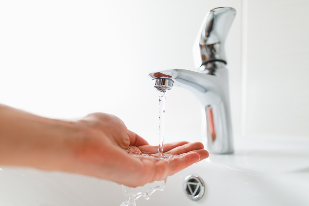 hand under faucet with a slow trickle because of a low water pressure issue
