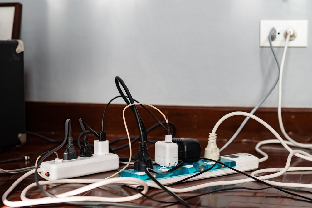 two surge protectors plugged into the wall outlet and each surge protector has several chargers plugged into them, showing a mess of cords